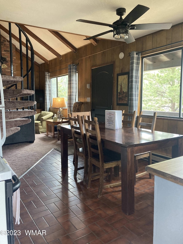 dining room featuring lofted ceiling with beams, a healthy amount of sunlight, and wooden walls