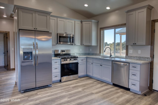 kitchen featuring lofted ceiling, light stone counters, stainless steel appliances, light wood-type flooring, and a sink