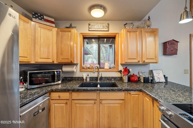 kitchen with a sink, stainless steel appliances, light brown cabinets, and dark stone counters