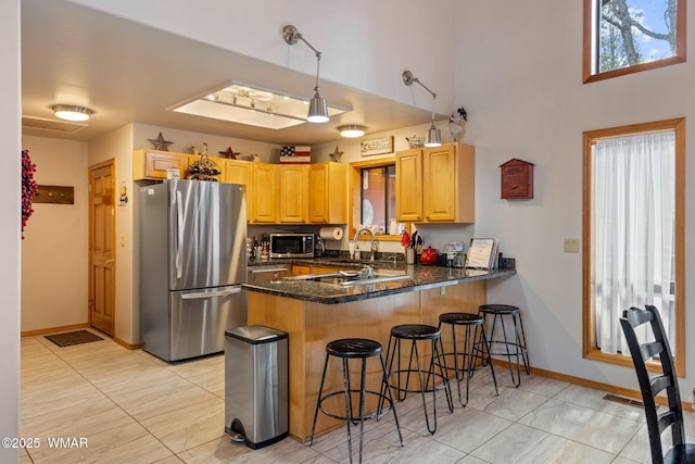 kitchen featuring a kitchen bar, dark stone countertops, a sink, appliances with stainless steel finishes, and a peninsula