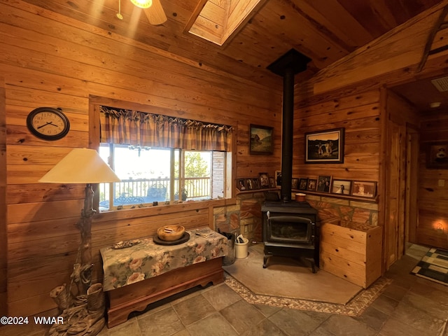 bedroom with vaulted ceiling with skylight, a wood stove, wooden ceiling, and wooden walls