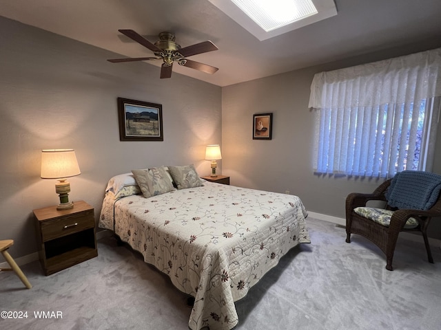 bedroom with a ceiling fan, light carpet, lofted ceiling with skylight, and baseboards