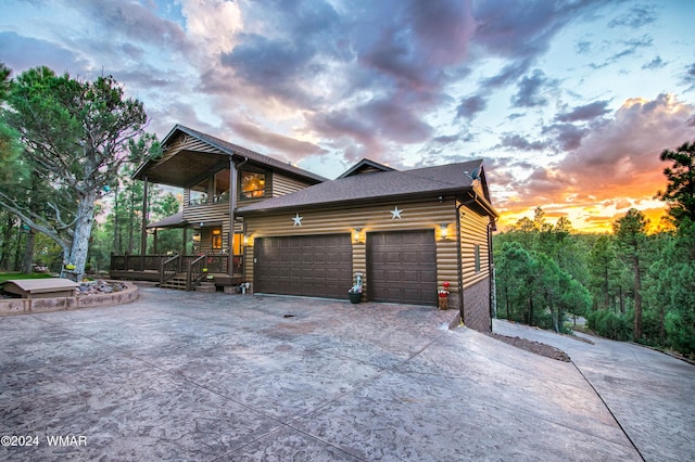 view of front of home featuring roof with shingles, concrete driveway, a balcony, a garage, and faux log siding