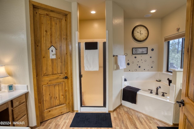 bathroom featuring a garden tub, recessed lighting, wood finished floors, vanity, and a stall shower