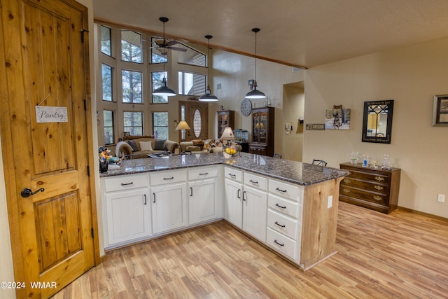 kitchen with open floor plan, white cabinets, hanging light fixtures, and dark stone countertops