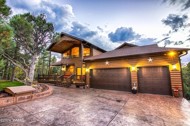 chalet / cabin featuring a deck, an attached garage, driveway, roof with shingles, and faux log siding