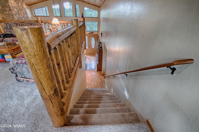 staircase with a textured wall, carpet floors, and high vaulted ceiling