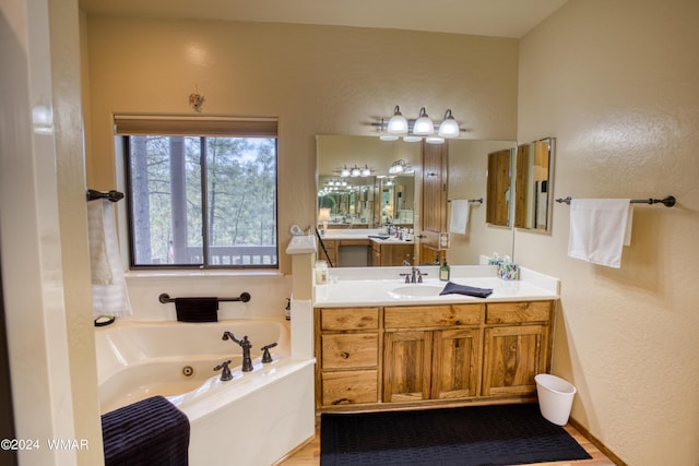 full bath with a textured wall, a jetted tub, and vanity