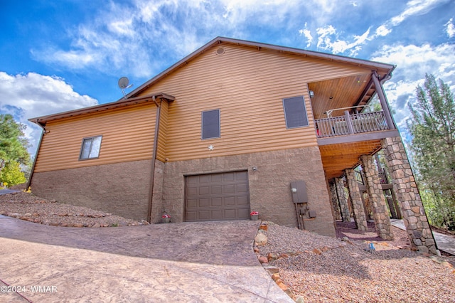 view of side of home featuring a garage, driveway, a balcony, and stucco siding