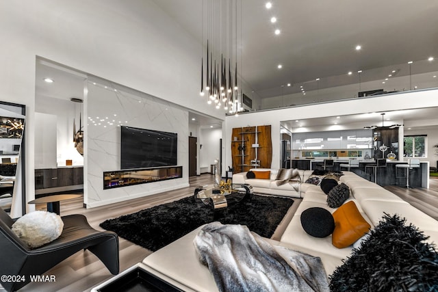 living area with a premium fireplace, wood finished floors, a towering ceiling, and recessed lighting