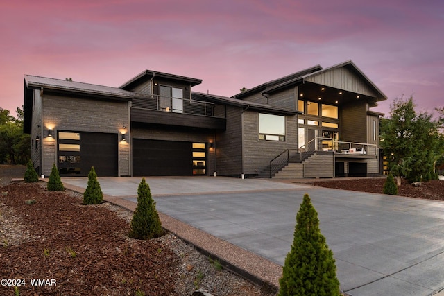 modern home featuring driveway, a balcony, an attached garage, and stairs