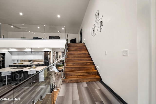 stairway with baseboards, wood finished floors, and recessed lighting