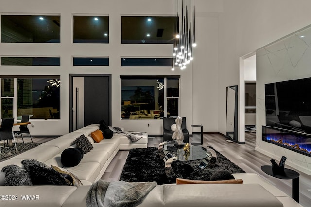 living room featuring a glass covered fireplace, light wood-style flooring, and a towering ceiling