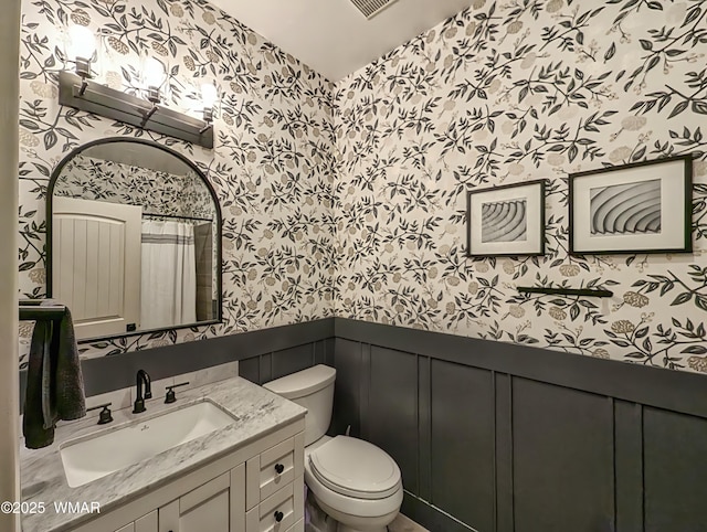 full bath featuring wallpapered walls, a wainscoted wall, toilet, a decorative wall, and vanity