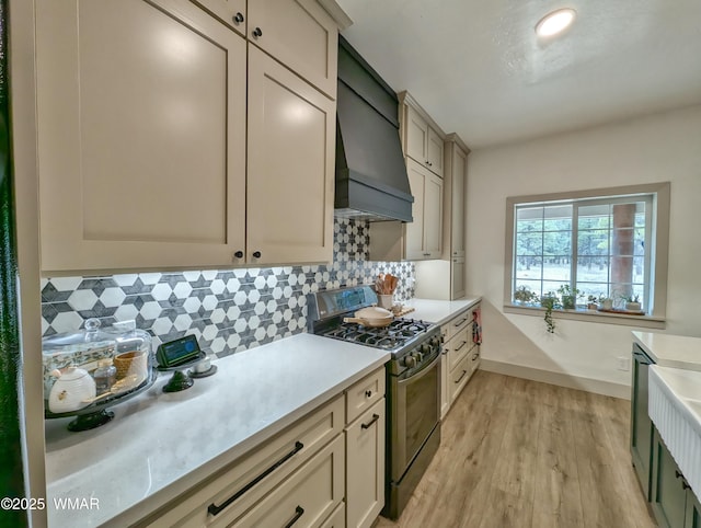 kitchen with custom exhaust hood, decorative backsplash, stainless steel gas range, and light countertops