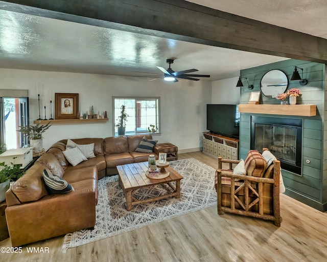 living room with ceiling fan, beamed ceiling, wood finished floors, and a fireplace