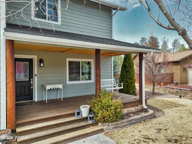 doorway to property featuring covered porch and a shingled roof