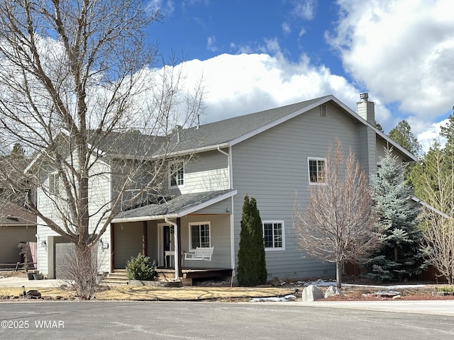 traditional-style home featuring a garage, a porch, and a chimney