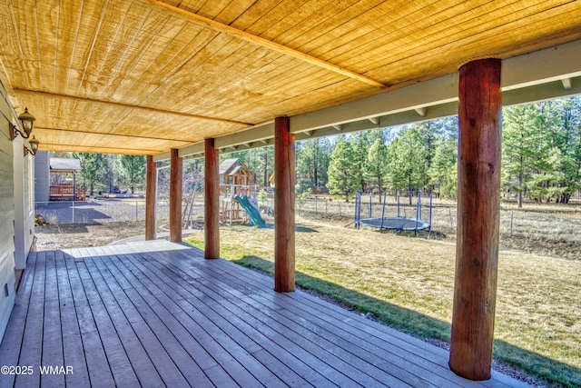 wooden terrace with a playground, a trampoline, fence, and a lawn