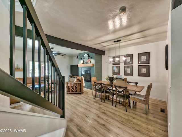 dining area with visible vents, stairway, ceiling fan with notable chandelier, wood finished floors, and a glass covered fireplace