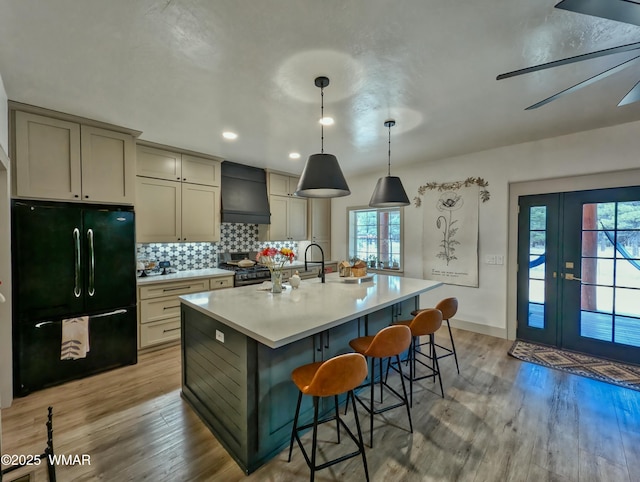 kitchen featuring custom exhaust hood, freestanding refrigerator, light wood-style floors, gas range, and tasteful backsplash