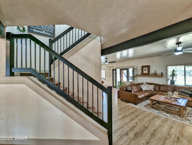 stairs with beam ceiling, wood finished floors, and a ceiling fan