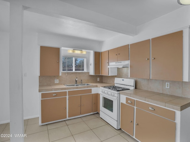 kitchen with under cabinet range hood, a sink, white gas range oven, tile counters, and decorative backsplash