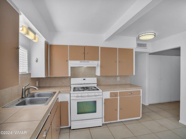 kitchen with under cabinet range hood, light countertops, backsplash, and white gas stove