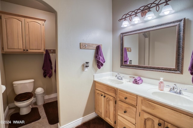 full bathroom with double vanity, a sink, toilet, and baseboards