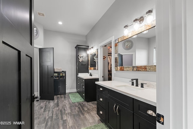 full bath featuring wood finished floors, two vanities, baseboards, and recessed lighting