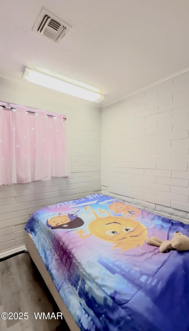 bedroom with visible vents, brick wall, and wood finished floors