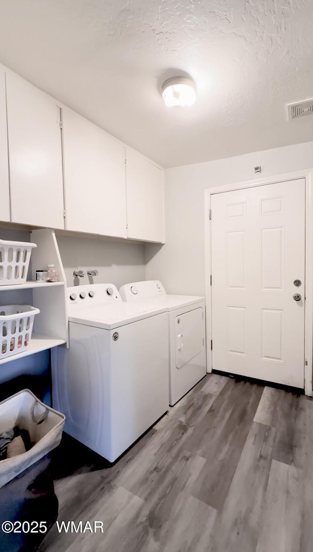 laundry area with cabinet space, visible vents, wood finished floors, independent washer and dryer, and a textured ceiling