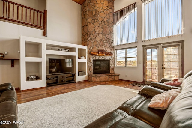 living room with a fireplace, a towering ceiling, wood finished floors, french doors, and baseboards