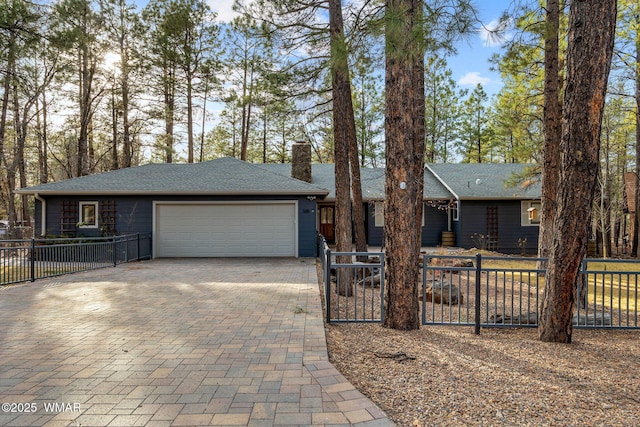 view of front of home featuring decorative driveway, roof with shingles, a chimney, fence, and a garage