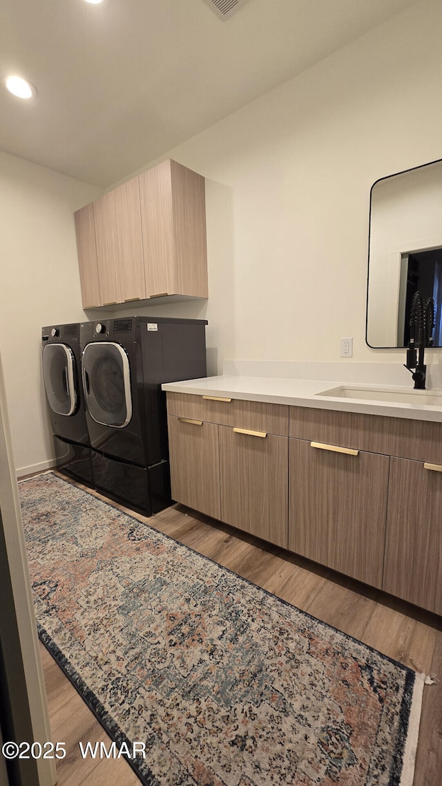 laundry room featuring visible vents, a sink, wood finished floors, cabinet space, and separate washer and dryer