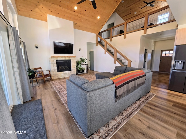 living room featuring wood finished floors, a ceiling fan, high vaulted ceiling, a stone fireplace, and wood ceiling