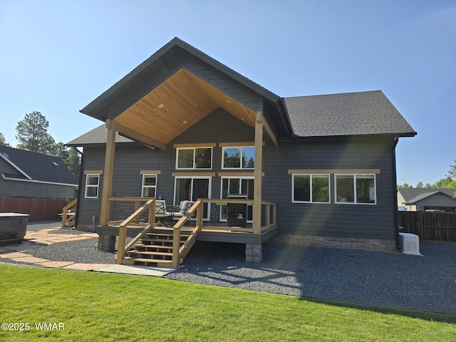 rear view of property featuring a yard, a deck, a shingled roof, and fence