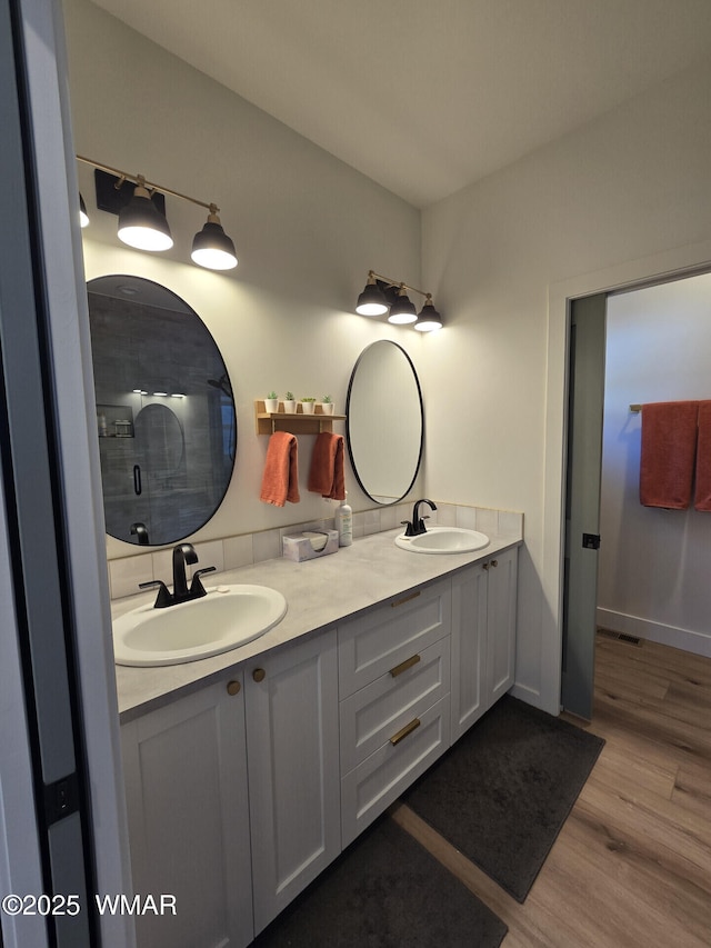 bathroom featuring double vanity, a tile shower, wood finished floors, and a sink