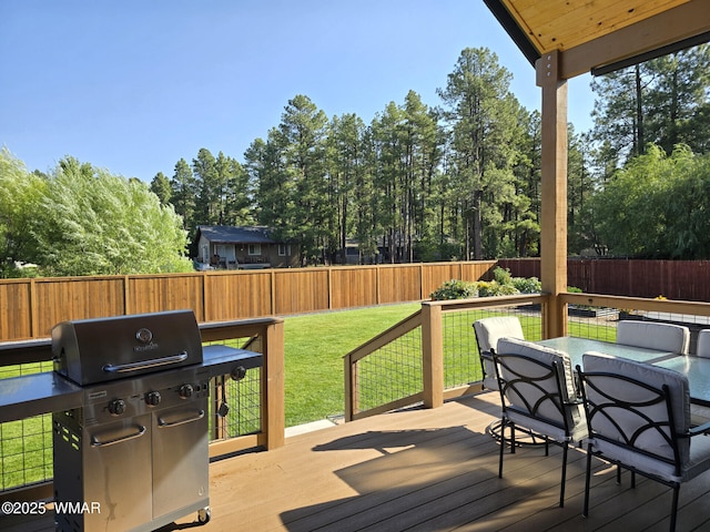 deck featuring outdoor dining area, a lawn, a fenced backyard, and a grill