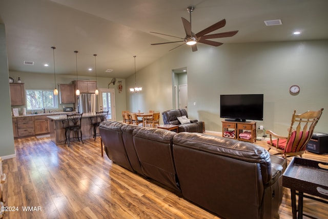 living area with visible vents, vaulted ceiling, wood finished floors, and ceiling fan with notable chandelier