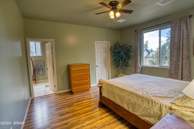 bedroom featuring visible vents, baseboards, ensuite bath, ceiling fan, and wood finished floors