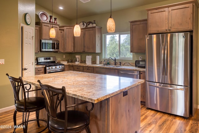 kitchen with light stone counters, a center island, pendant lighting, appliances with stainless steel finishes, and a sink