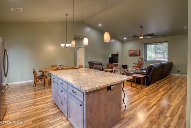 kitchen featuring light wood-style flooring, light stone counters, open floor plan, a center island, and decorative light fixtures