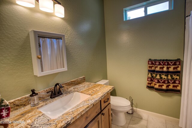 bathroom featuring toilet, a textured wall, baseboards, and vanity