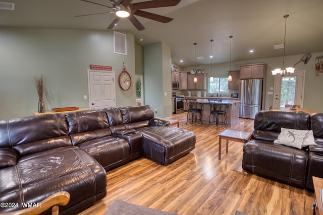 living area with light wood-style floors, visible vents, vaulted ceiling, and ceiling fan with notable chandelier