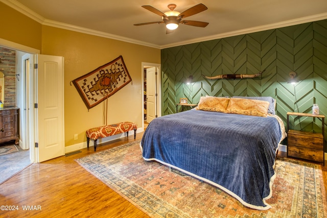 bedroom with baseboards, an accent wall, wood finished floors, and crown molding