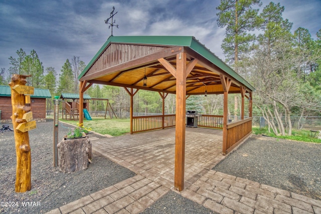 view of patio with playground community, a gazebo, a grill, fence, and driveway