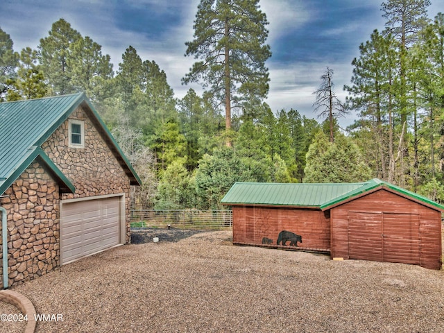 view of side of home featuring a garage, fence, metal roof, and an outdoor structure