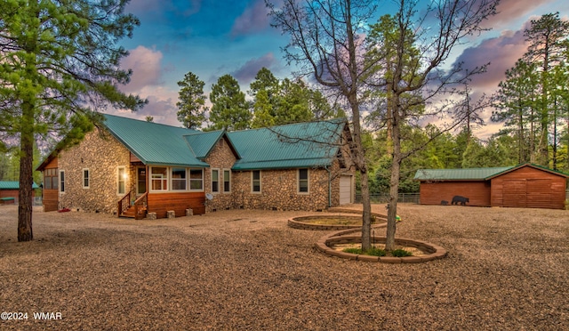 view of front of property with a garage, driveway, stone siding, metal roof, and an outbuilding