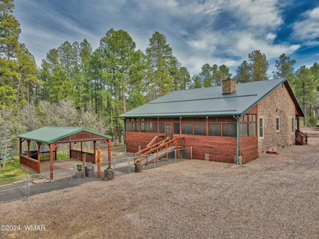 chalet / cabin with a chimney, metal roof, fence, a carport, and stone siding